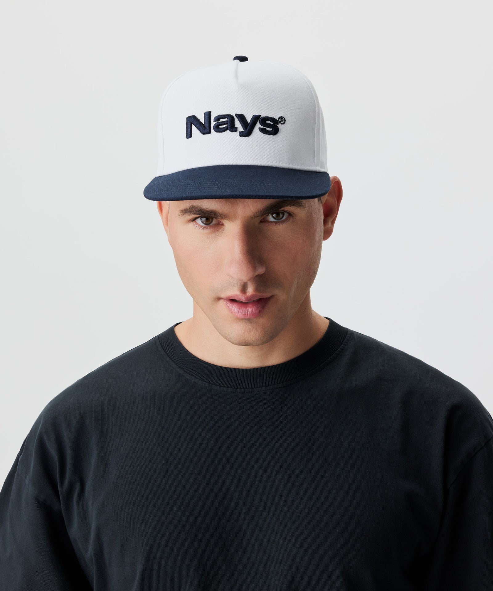 Frontansicht Mann mit Cap. Die Cap ist weiß mit blauem Schirm und einem blauen Nays-Logo Strick.