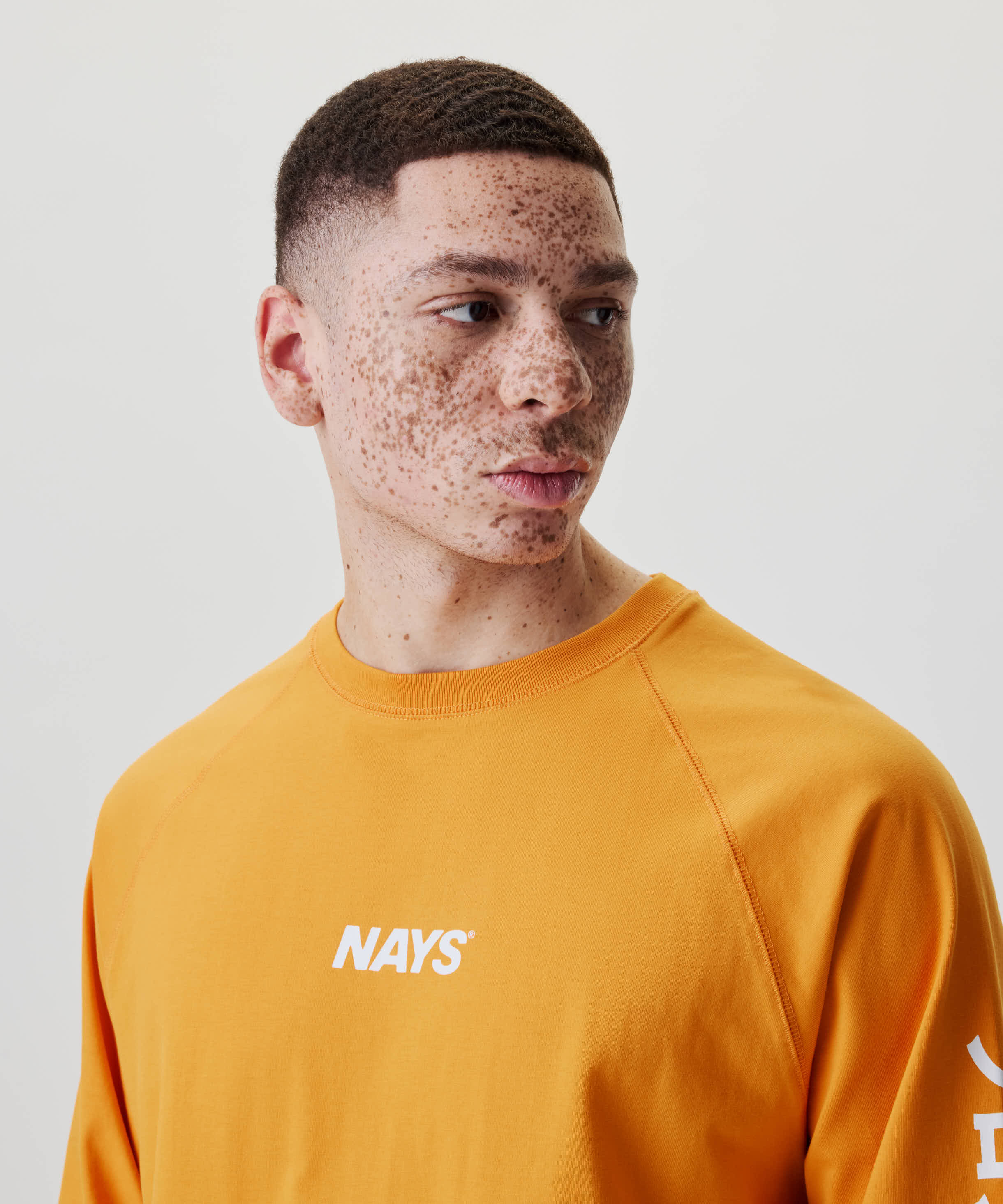 Porträt eines jungen Menschen im Nays Pro Tackle International Longsleeve mit markantem Logo-Print und sportlichen Raglanärmeln, betont durch dezente Naht-Details.