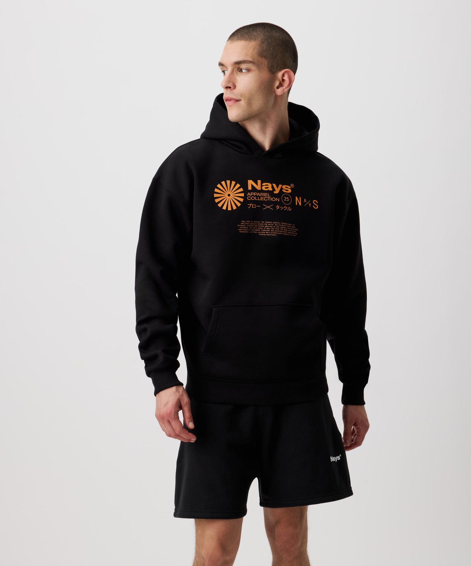 Ein schwarzer Kapuzen-Pullover mit kontrastreichen Prints in einem leuchtenden Orange, getragen von einem Mann. Der Print besteht aus einem runden, sonnenartigen Symbol und daneben tonale Nays Logo Schriftzüge.