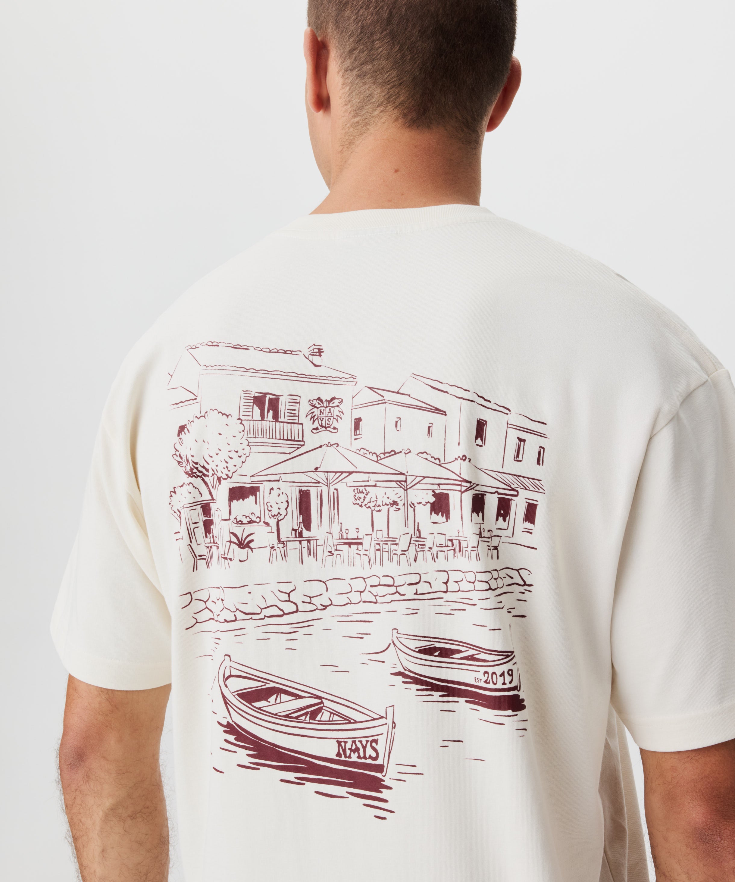 Rückansicht Mann im beige-farbigem T-shirt mit großem Print auf dem Rücken.
