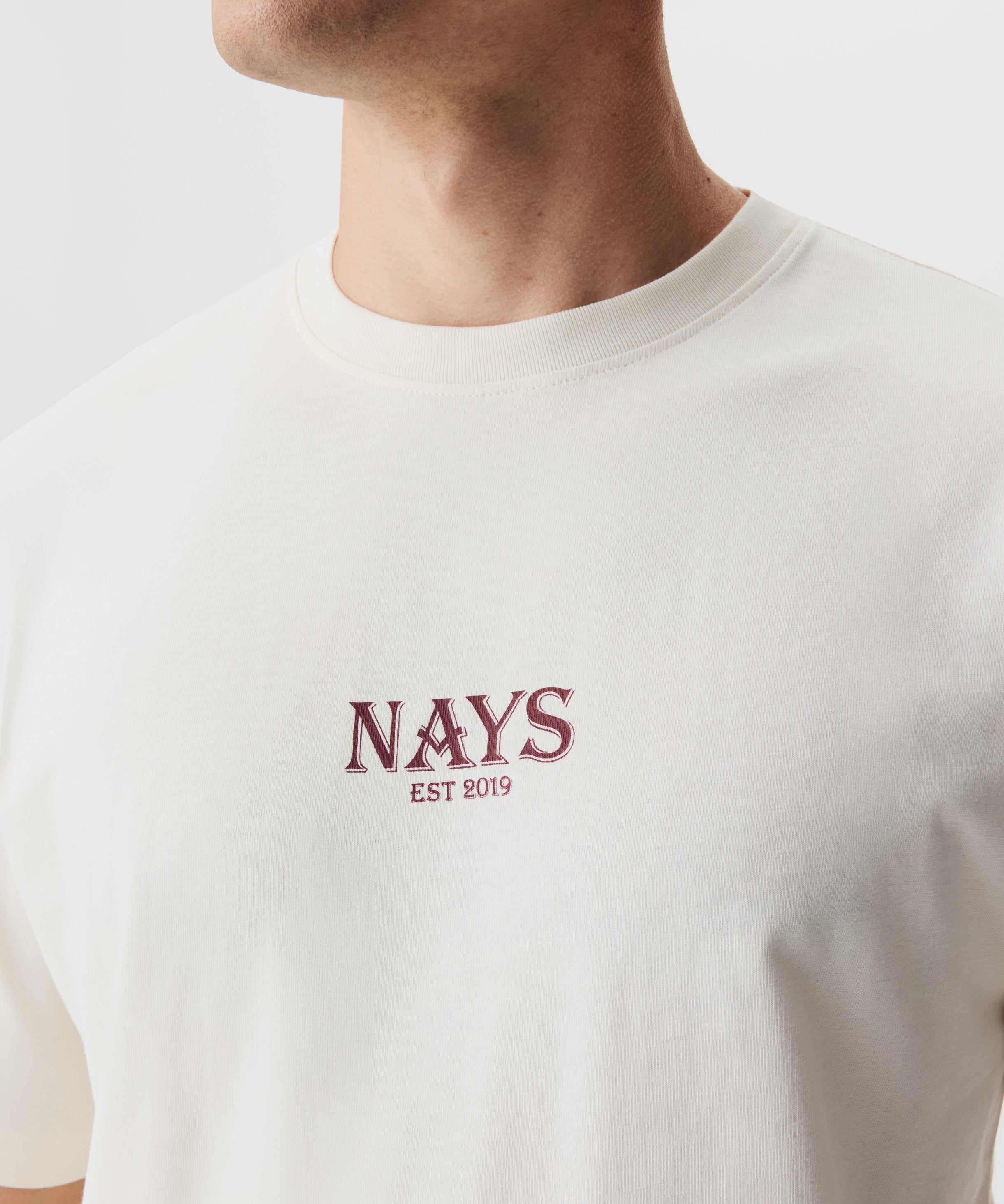 Detailansicht Mann im beige-farbigem T-shirt mit rotem Nays Logo Schriftzug.
