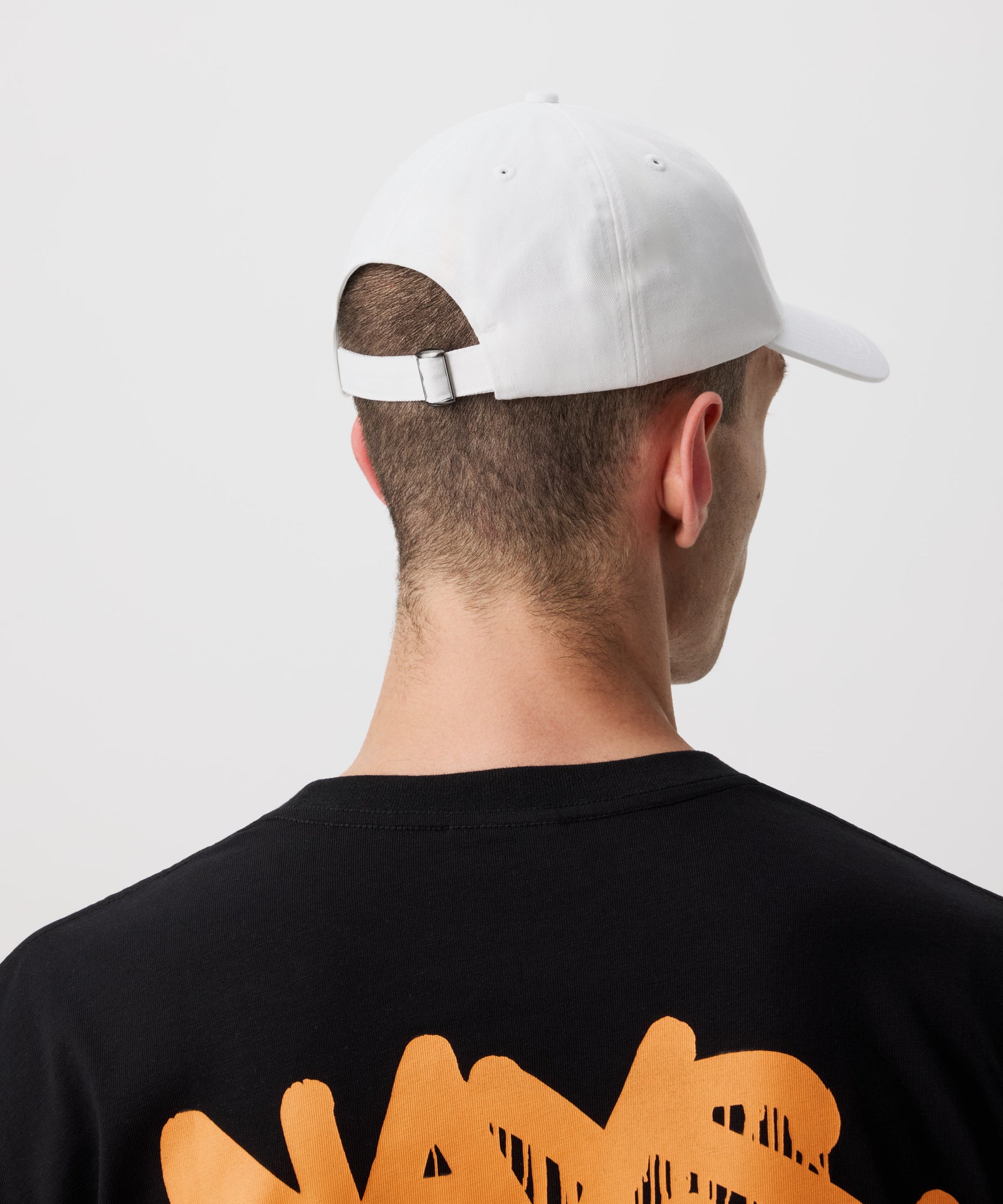 Zu sehen ist eine weiße Schirm Mütze von hinten getragen von einem Mann- er trägt dazu ein schwarzes T-Shirt mit orange-farbigem Logo.