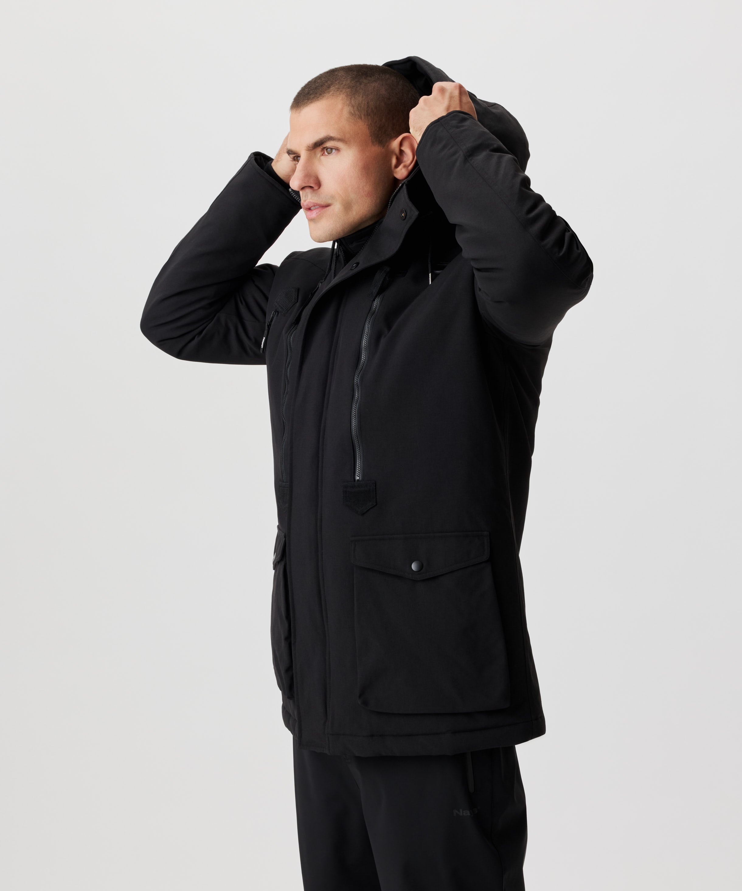 Seitliche Frontansicht Mann setzt eine Kapuze eines schwarzen Winter-Parkas auf.