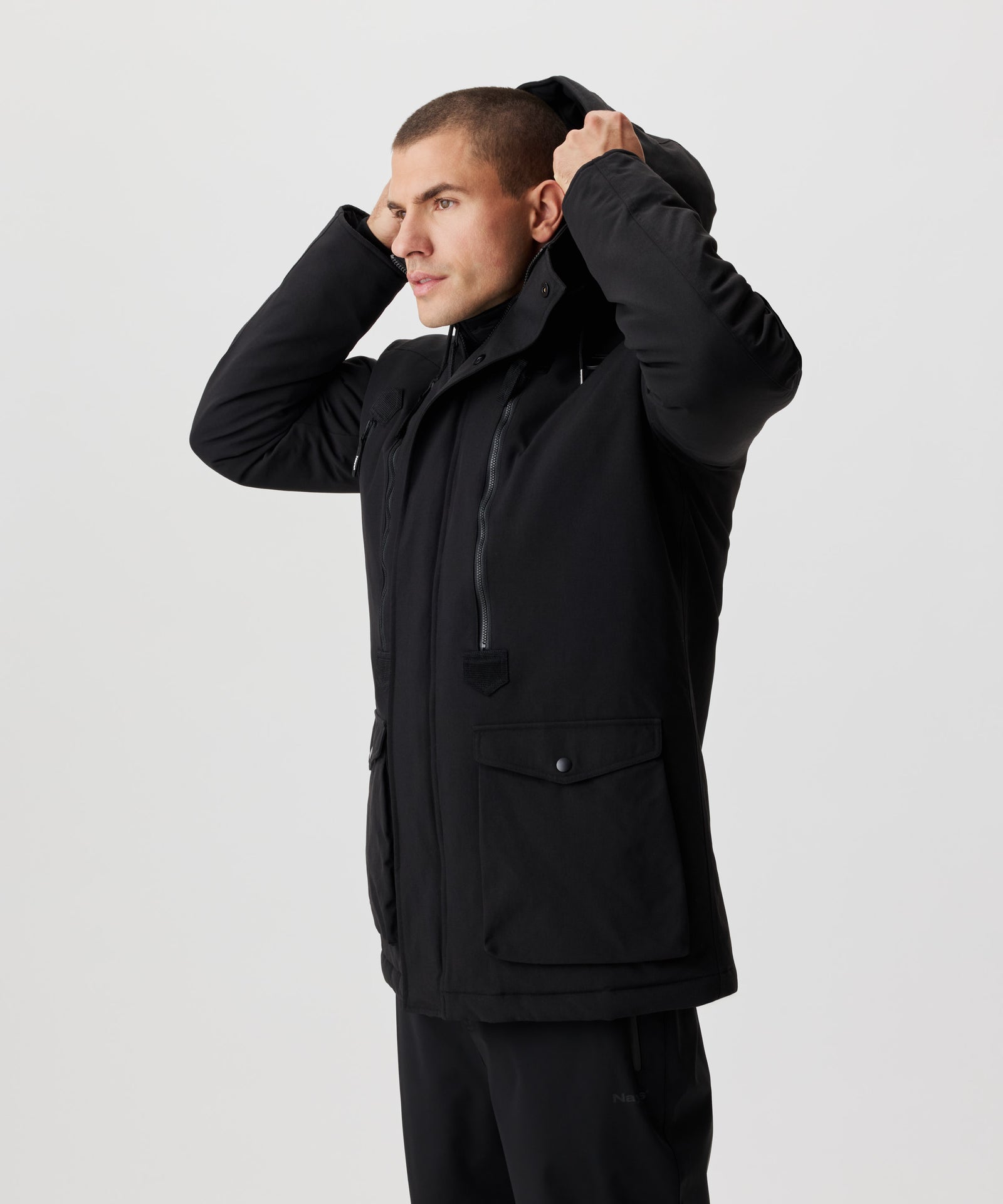 Seitliche Frontansicht Mann setzt eine Kapuze eines schwarzen Winter-Parkas auf.