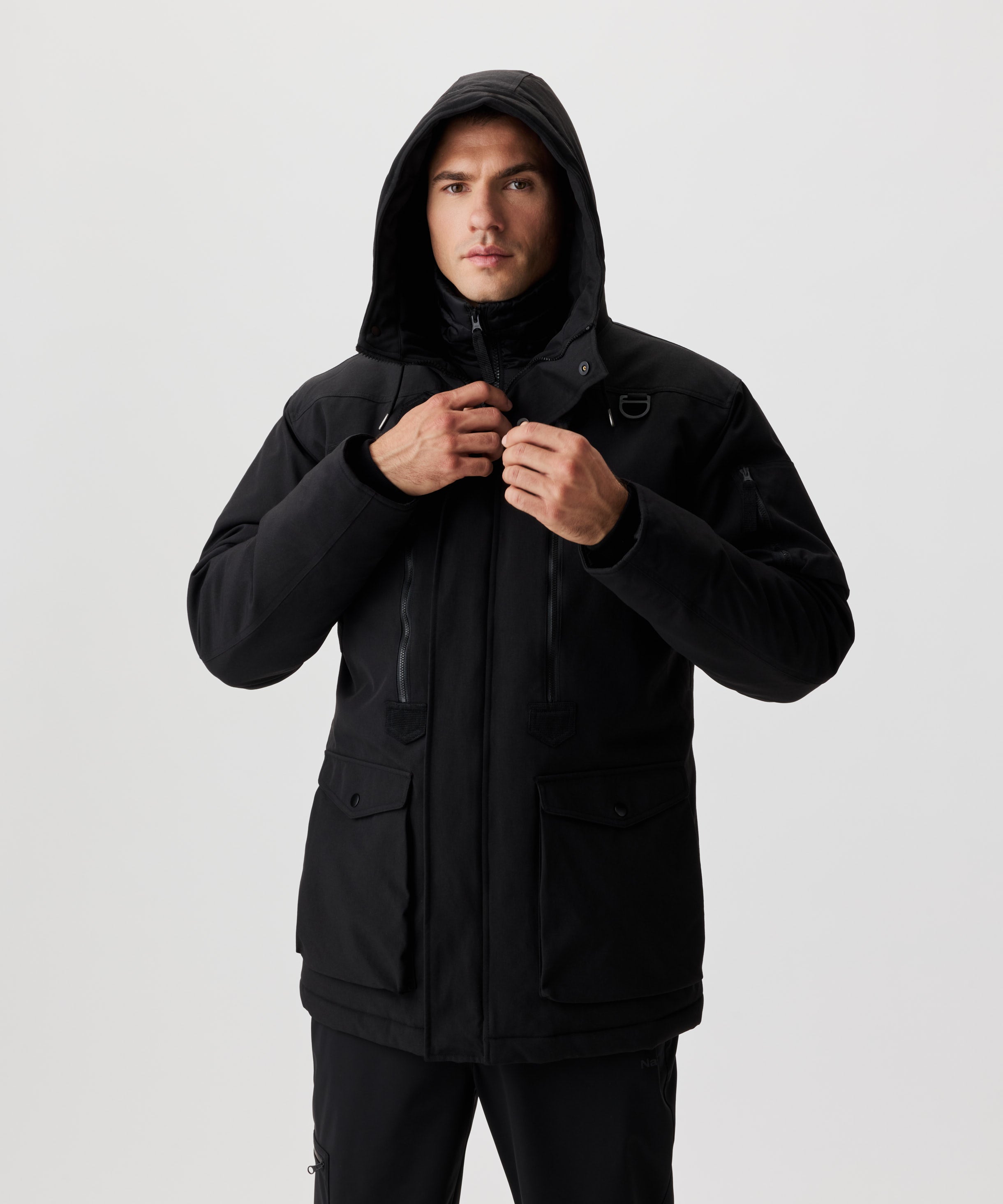 Frontansicht Mann im schwarzen Winter-Parka schliesst den hoch-stehenden Kragen.