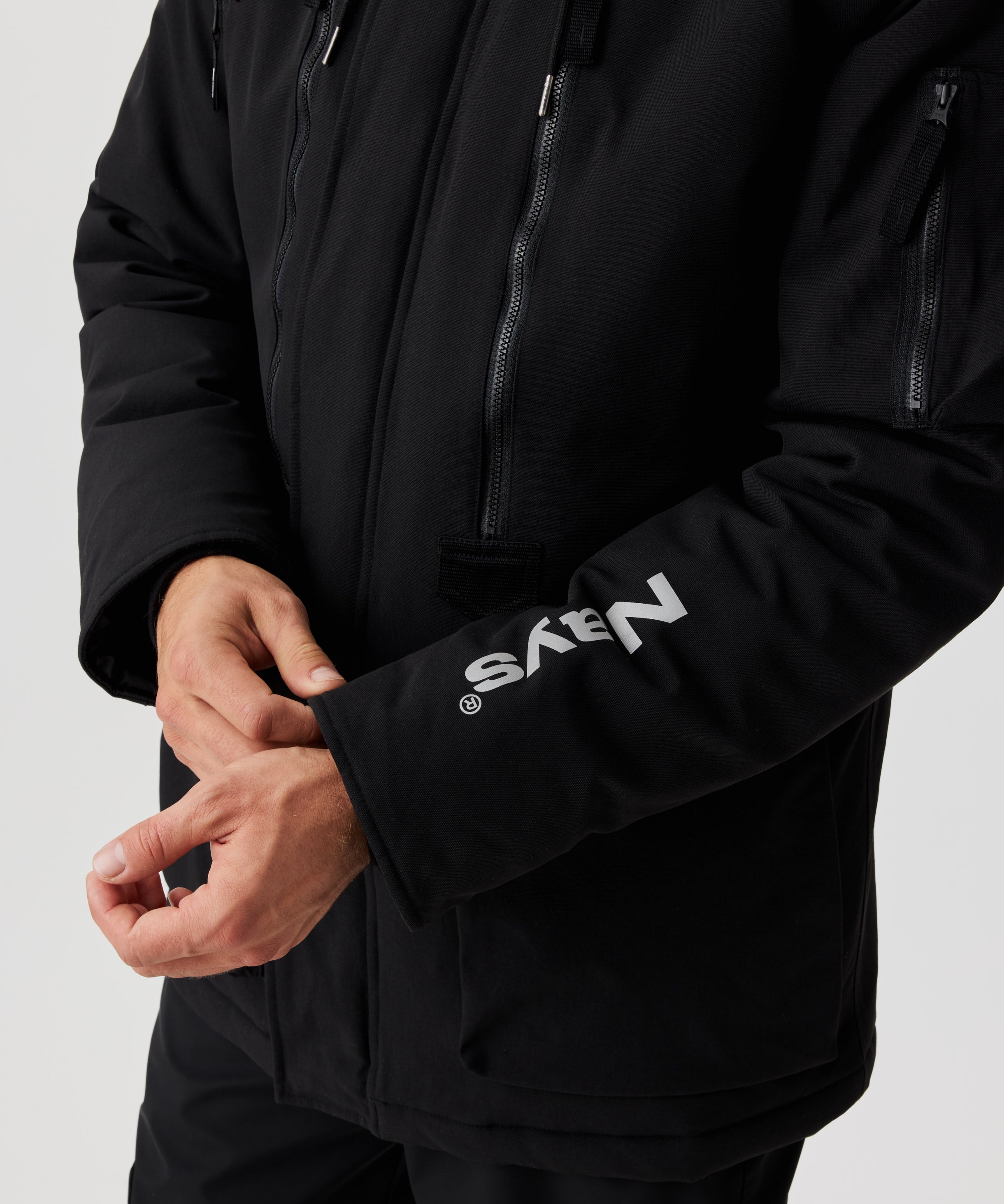 Ein Mann zieht am Bündchen einer schwarzen Winterjacke. Ein großes Nays-Logo auf dem linken Ärmel ist zu sehen.