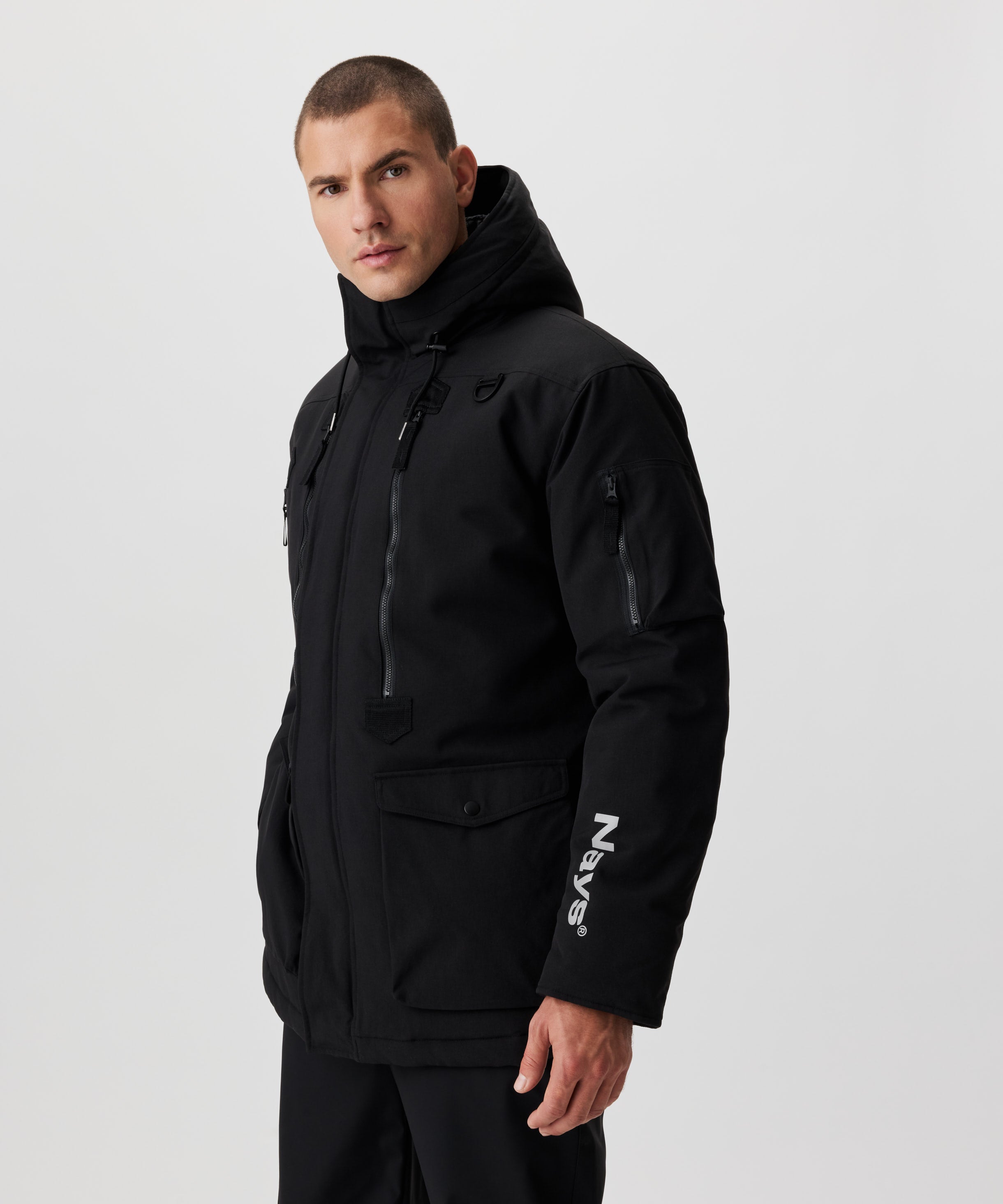 Seitliche Frontansicht Mann im schwarzen Winter-Parka. Auf dem linken Ärmel erkennt man ein weißes Nays-Logo.