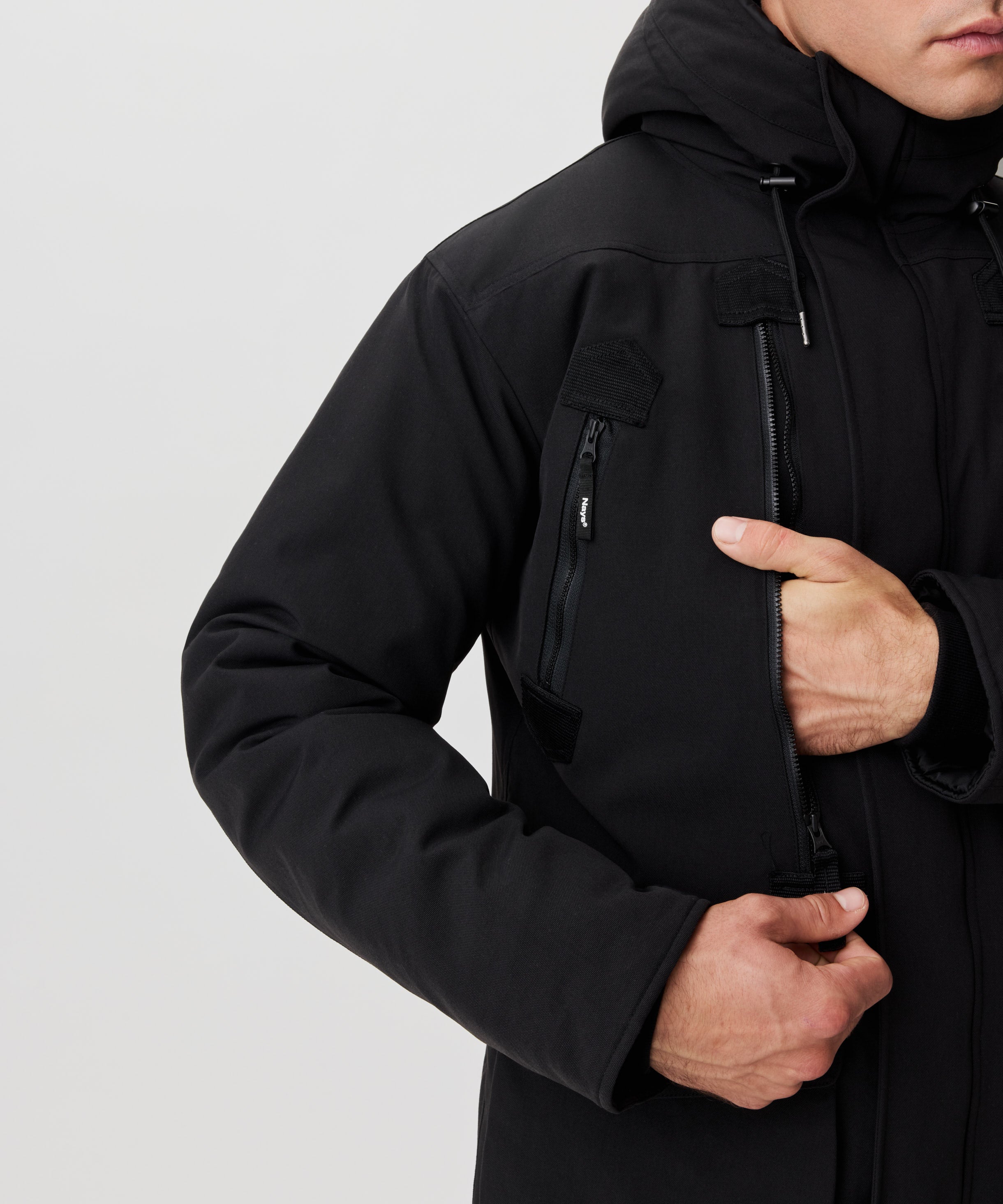 Man greift in eine große Brusttasche einer schwarzen Winterjacke mit Kapuze.