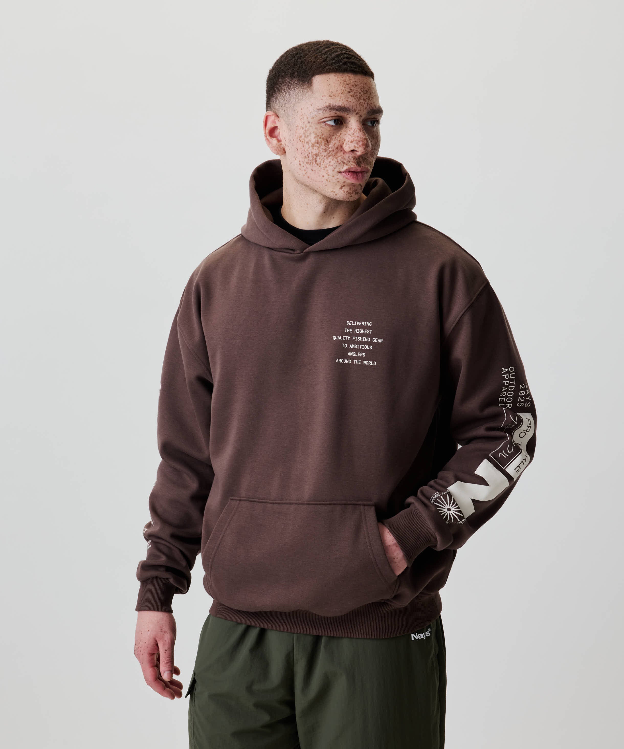 Junger Mann trägt den Nays Quote Hoodie mit weißen Grafiken und Text, kombiniert mit olivgrüner Hose. Perfekt für Komfort und Alltag.