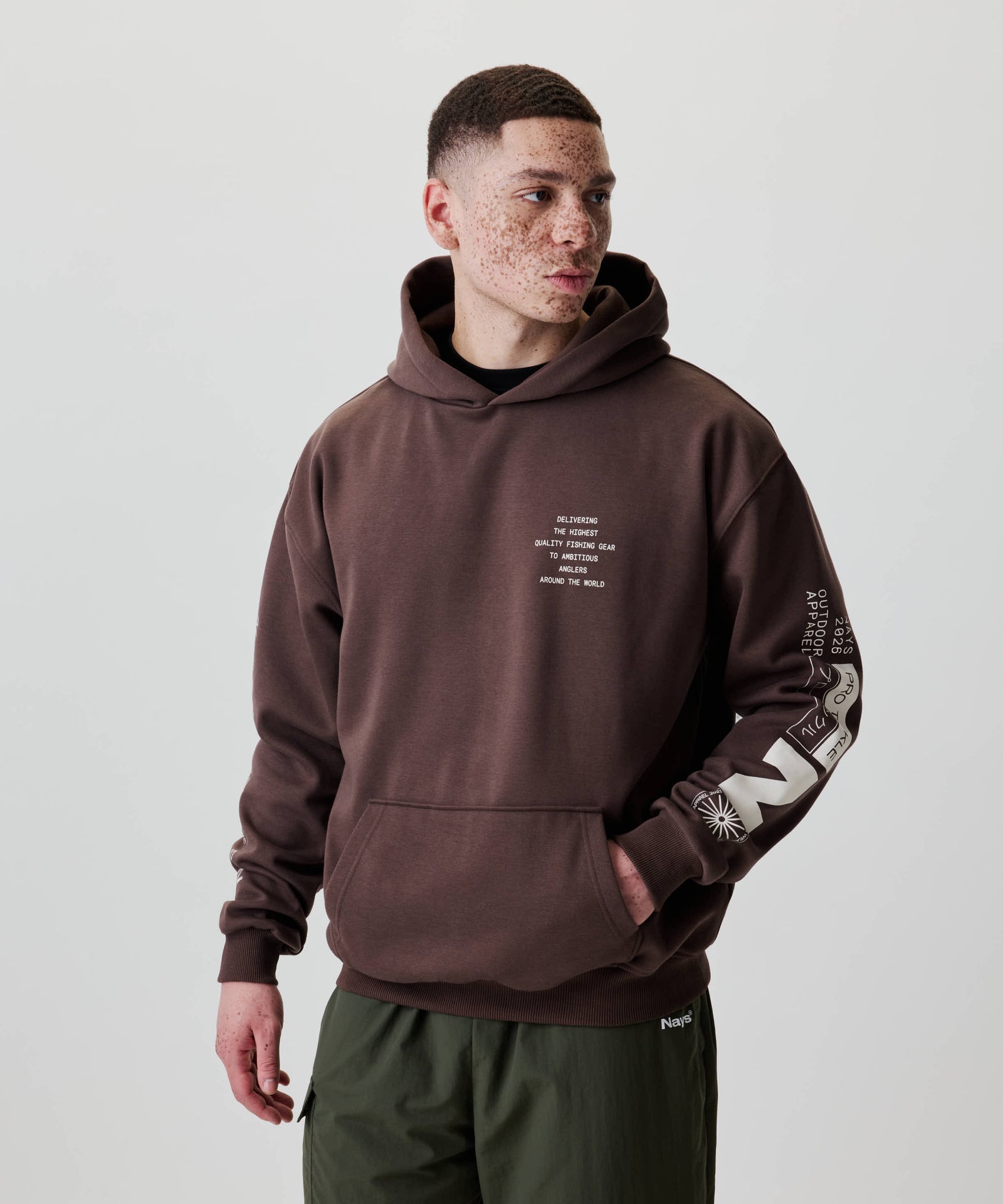 Junger Mann trägt den Nays Quote Hoodie mit weißen Grafiken und Text, kombiniert mit olivgrüner Hose. Perfekt für Komfort und Alltag.