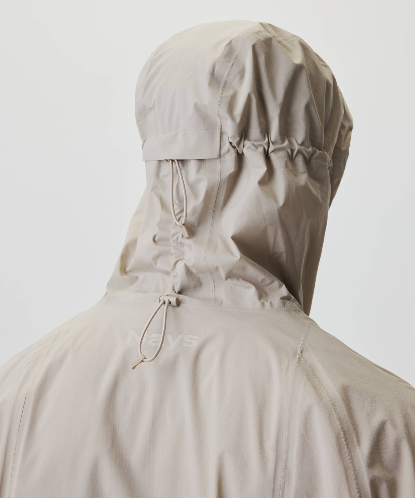 Rückansicht der Nays 2L Defend Mono Jacket mit verstellbarer Kapuze, elastischen Nähten und Logo, zeigt funktionales Design und wasserabweisendes Material.