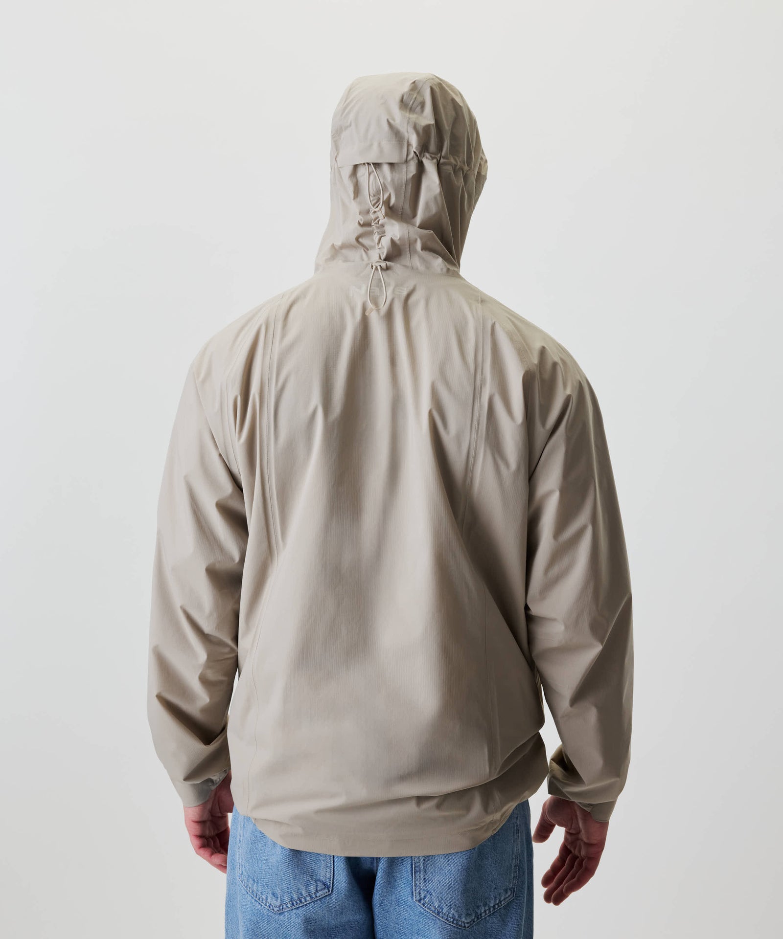 Rückansicht der Nays 2L Defend Mono Jacket mit verstellbarer Kapuze, sportlichen Raglanärmeln und elastischen Bündchen, getragen über mittelblauen Jeans.