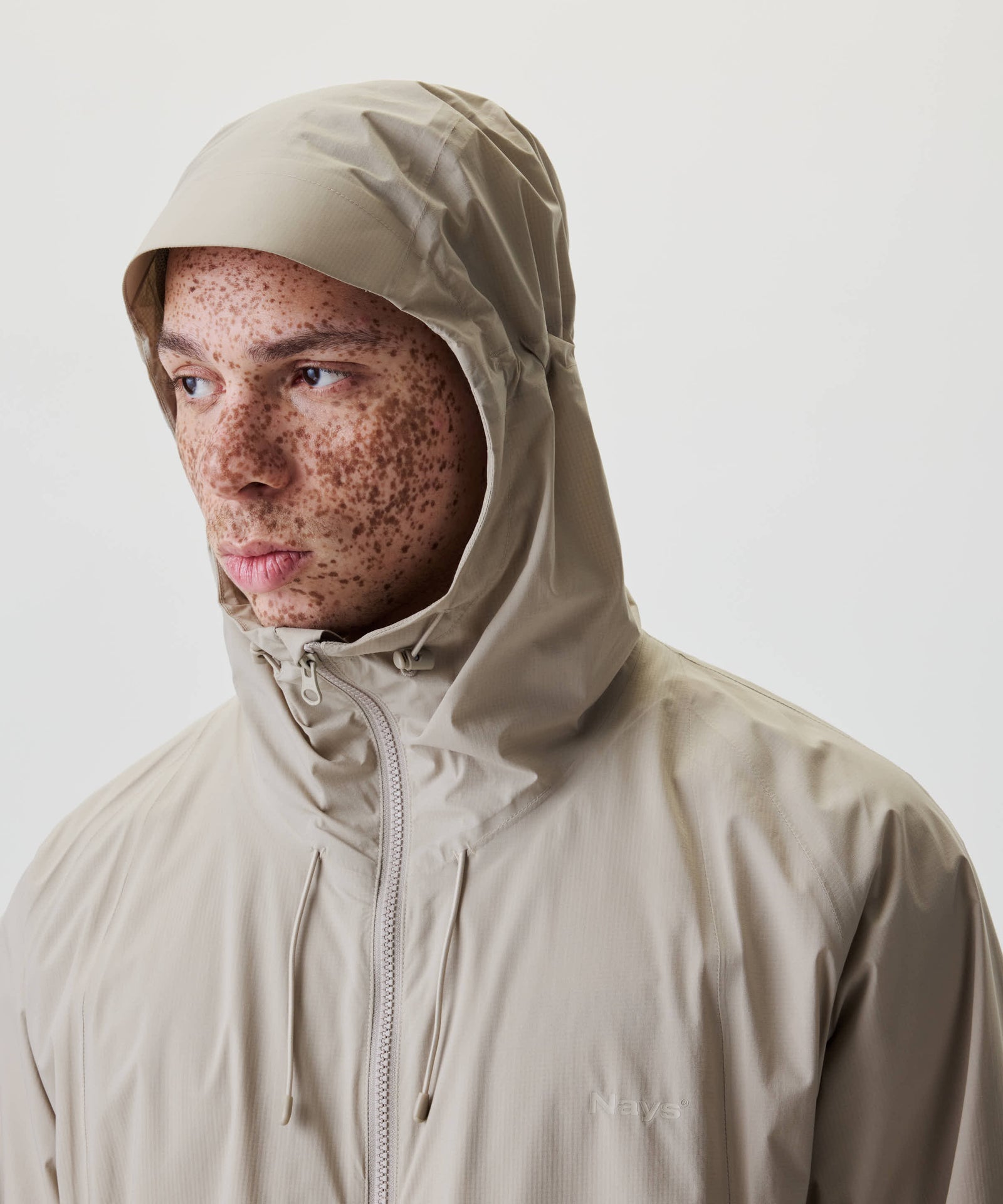 Nahaufnahme eines jungen Mannes mit Sommersprossen, der die Nays 2L Defend Mono Jacket mit verstellbarer Kapuze trägt, ideal für Outdoor-Aktivitäten und wechselhaftes Wetter.