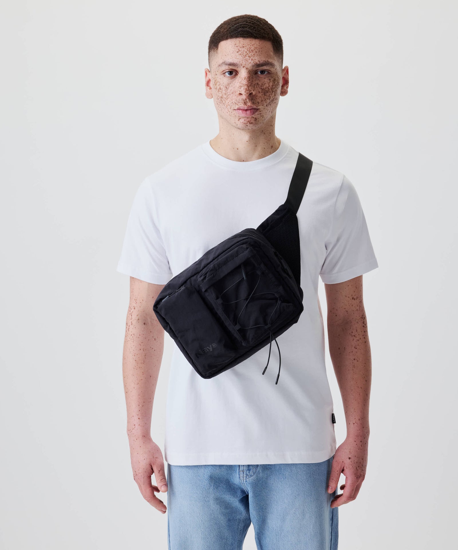 Person mit Nays Utility Cross Body Bag 2.0, schwarzer rechteckiger Taschenform, Front-Reißverschlusstasche, Kordeldetail, bietet funktionalen Stauraum und verstellbares Nylonband.