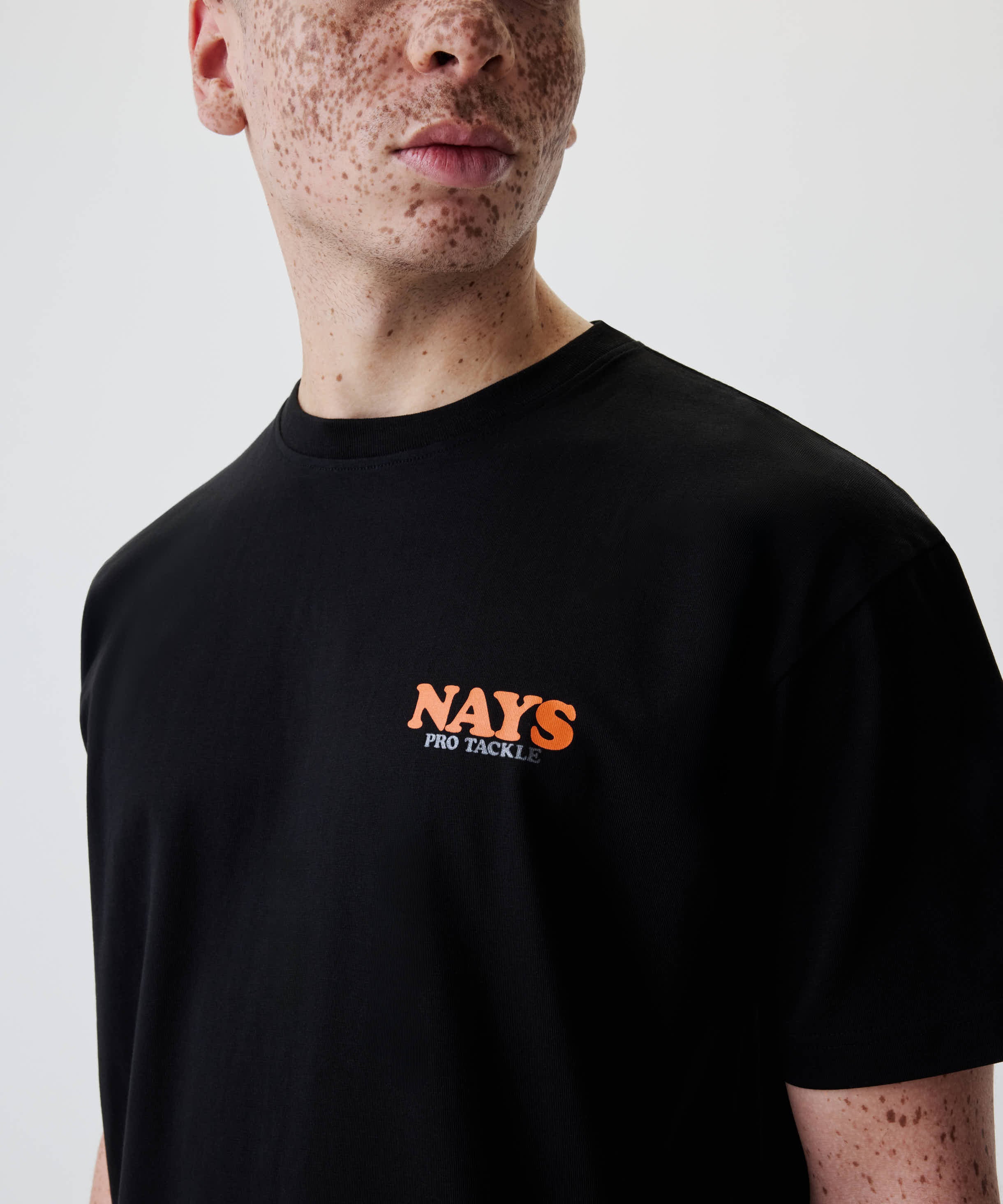 Nays College Print Tee in Schwarz mit orangefarbenem NAYS Logo und PRO TACKLE in Weiß auf der Brust, aus 100% Baumwolle, freizeittauglich.