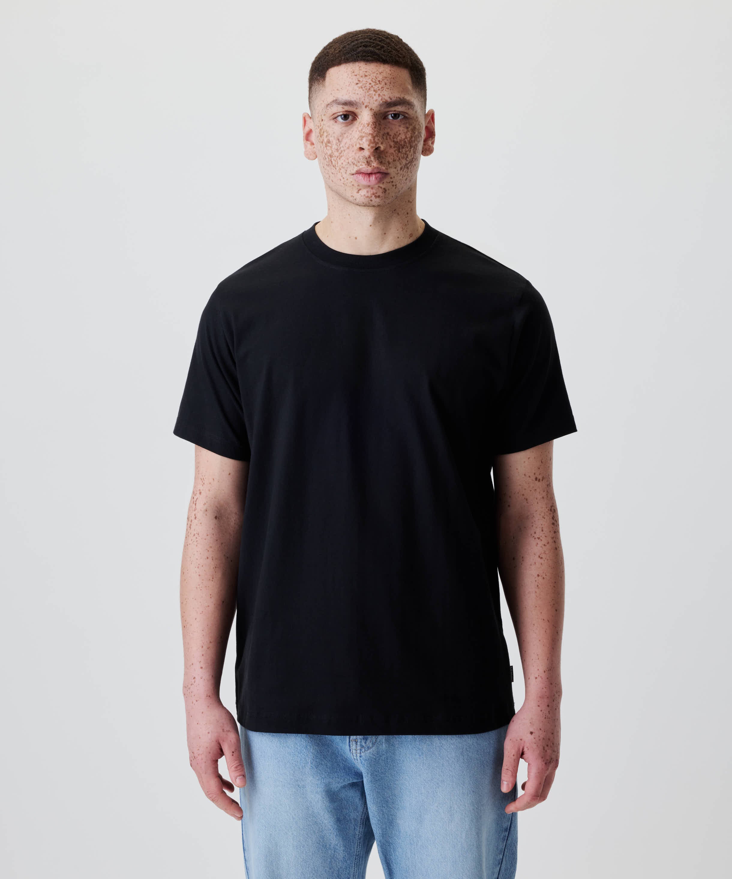 Person trägt das Nays Classic Regular Flag Tee in Schwarz, Regular-Fit für klassische Silhouette, ergänzt durch ein dezentes Flag Label, geeignet für den Alltag.