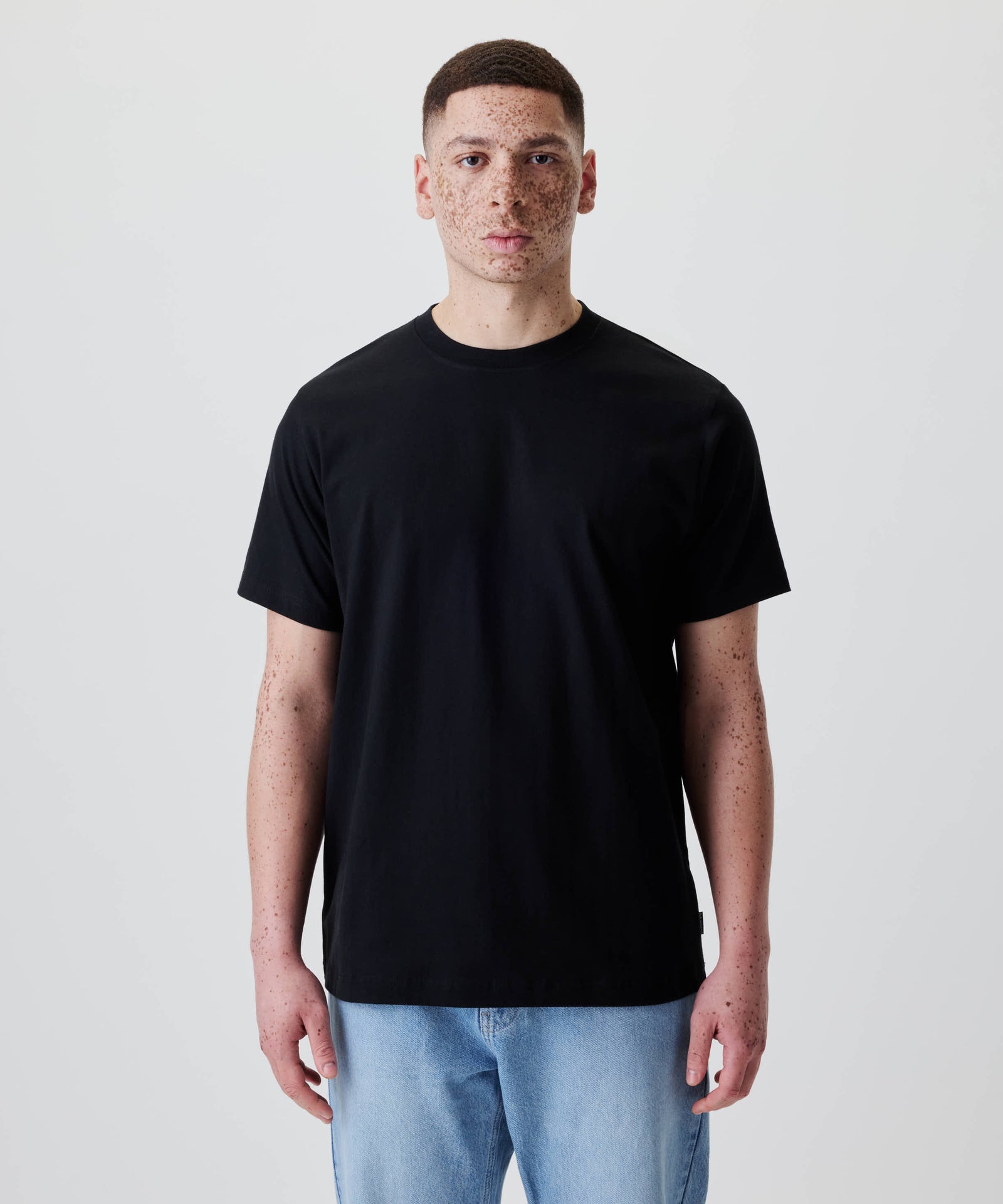 Person trägt das Nays Classic Regular Flag Tee in Schwarz, Regular-Fit für klassische Silhouette, ergänzt durch ein dezentes Flag Label, geeignet für den Alltag.