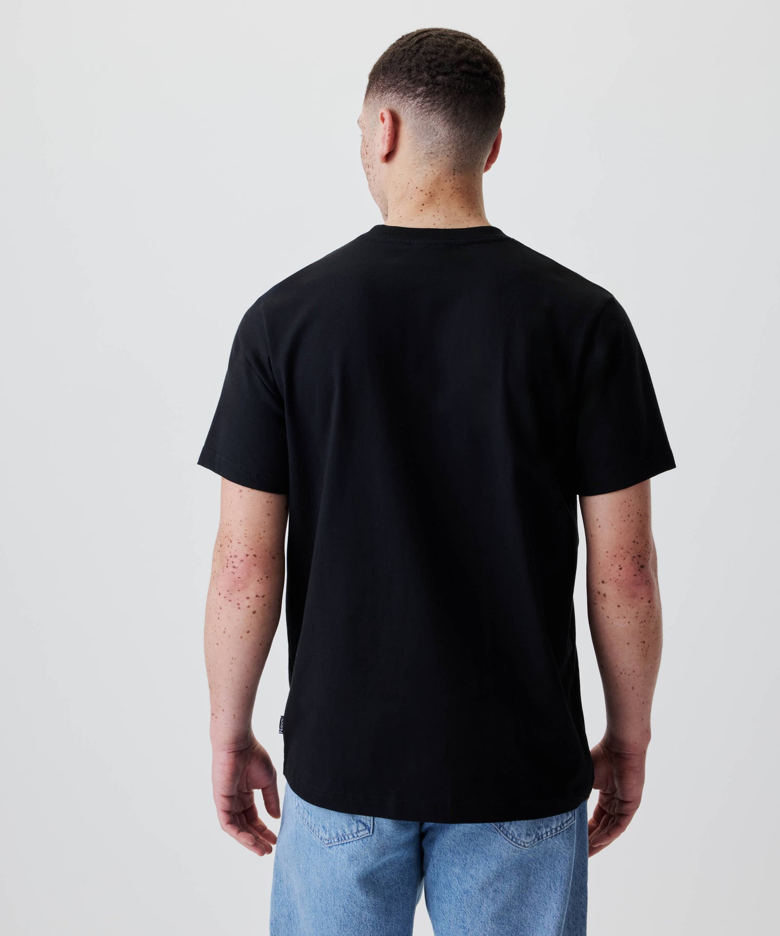 Person von hinten in schwarzem Nays Classic Regular Flag Tee und hellblauen Jeans, schlichtes Design, Regular-Fit für klassischen Sitz.