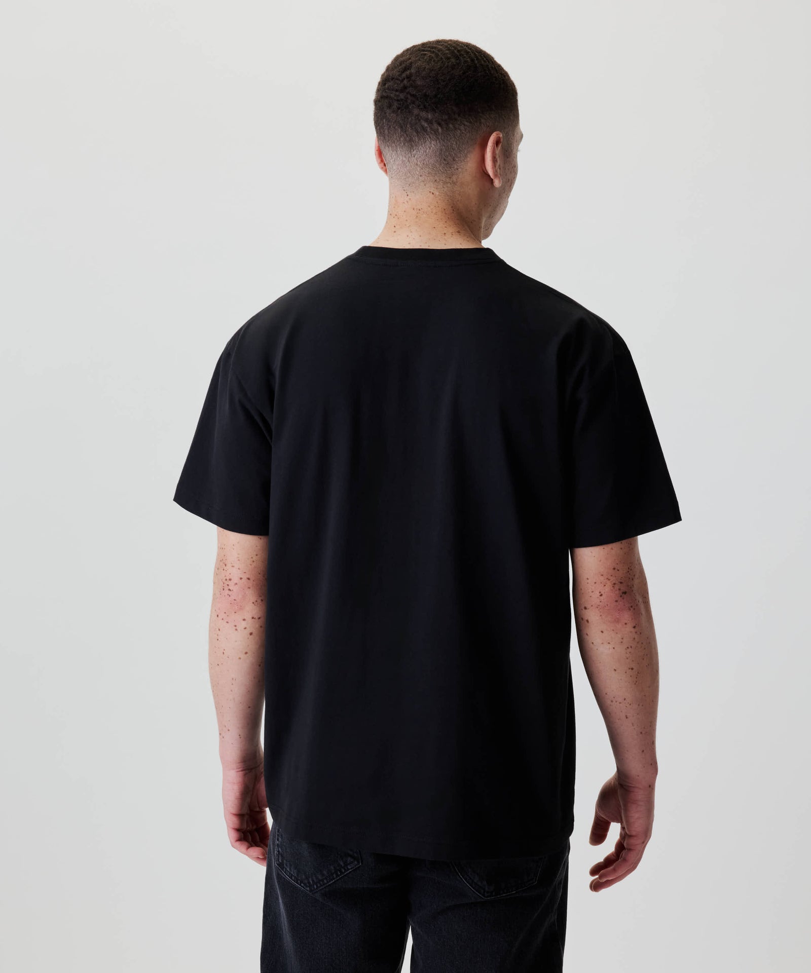 Rückansicht einer Person im Nays Loose Fit Chest Print Tee, schwarz, mit entspanntem Schnitt. Das Shirt zeigt keine sichtbaren Drucke auf der Rückseite.