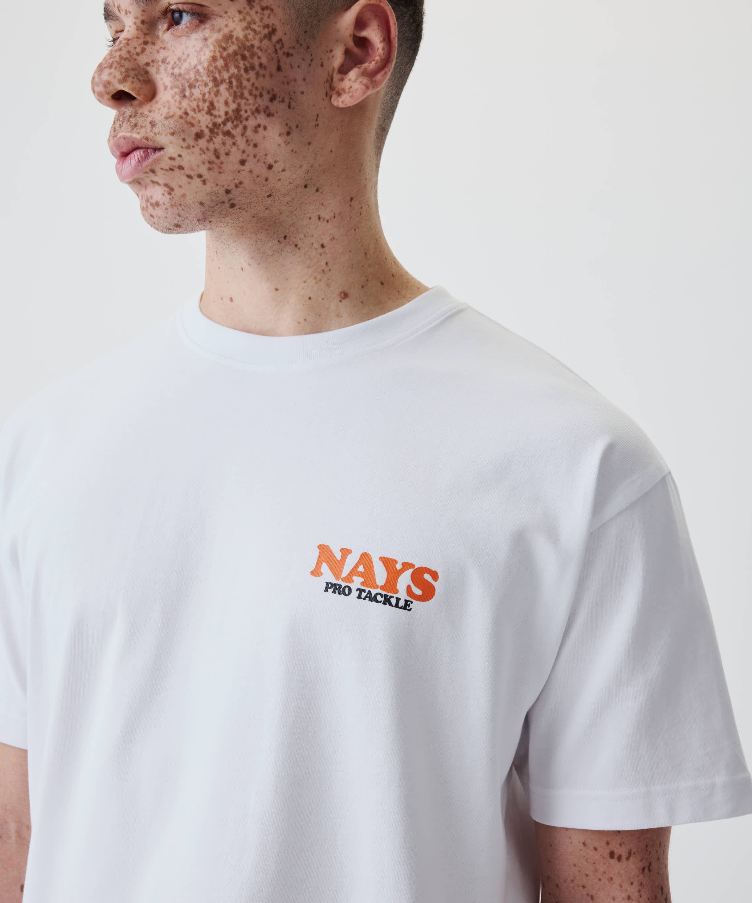 Person trägt das Nays College Print Tee in Weiß mit kleinem Logo NAYS PRO TACKLE auf der Brust. 