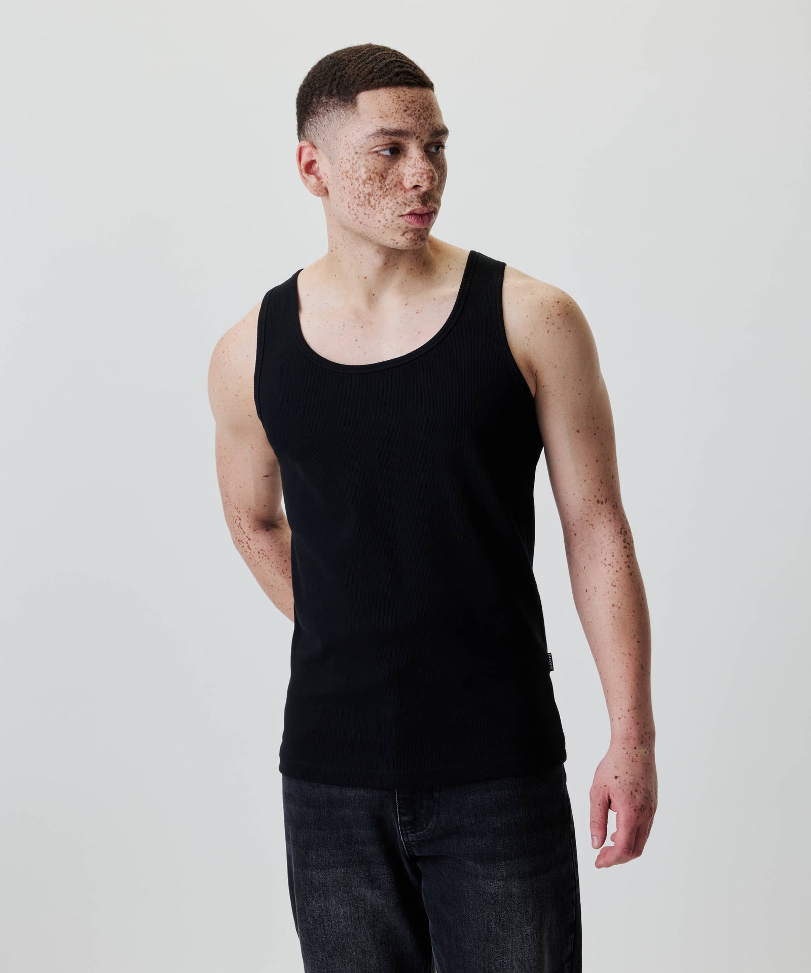 Ein junger Mann trägt ein Nays Classic Rib Tank Top in Schwarz, aus 100 % Baumwolle, mit einem dezenten Nays Flag Label, ideal für den Alltag.