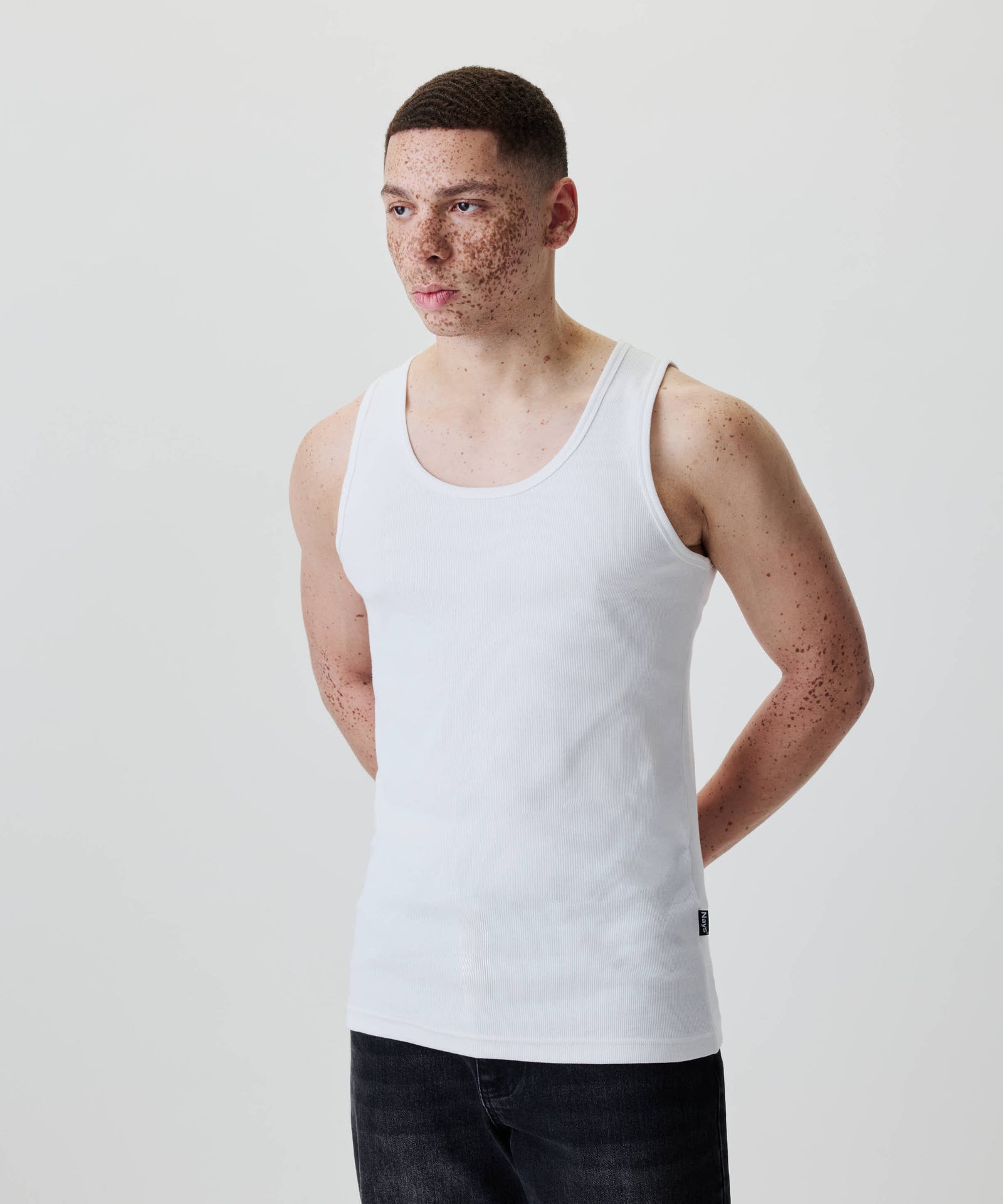 Ein junger Mann trägt das Nays Classic Rib Tank Top, ein weißes, eng anliegendes Baumwoll-Rippoberteil, ideal für entspannte Alltagslooks.
