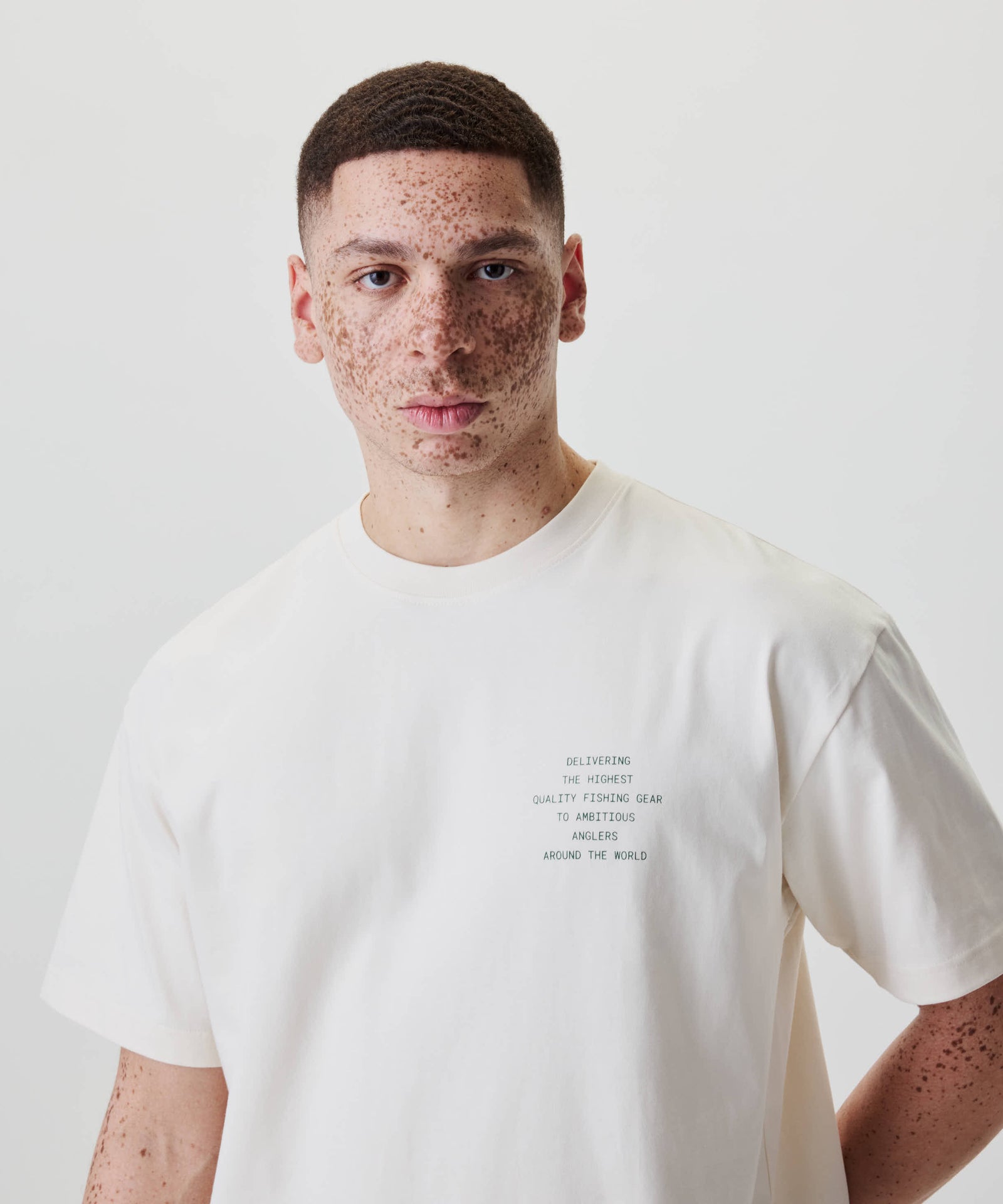 Junger Mann mit Sommersprossen trägt das Nays Quote Tee, locker geschnittenes Off White-Shirt mit dunkelgrünem Text. Ideal für entspannte Freizeitlooks.