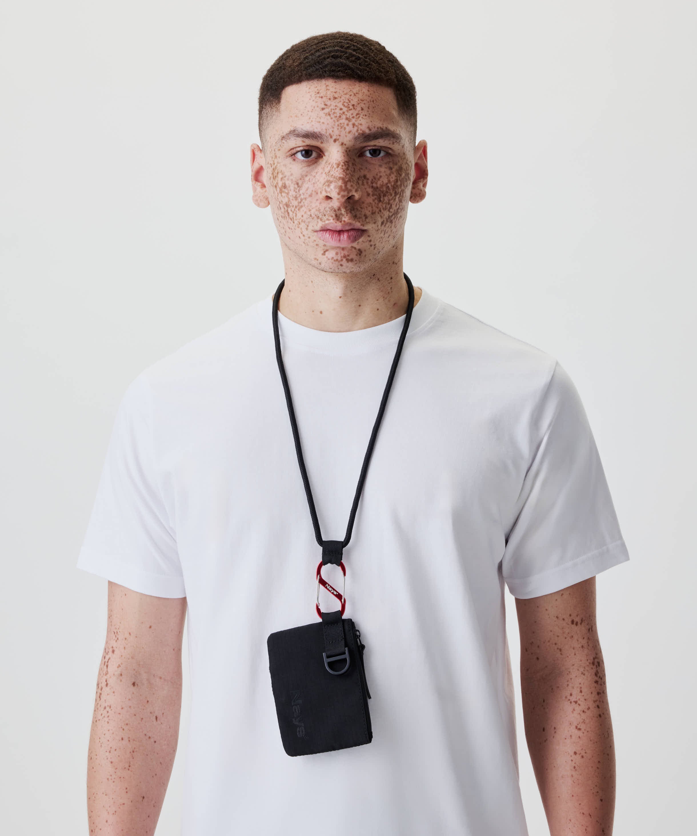 Ein junger Mann trägt das Nays Neck Pouch aus Ripstop, mit Reißverschlussfach und Mesh-Tasche, an einem schwarzen Band um den Hals.