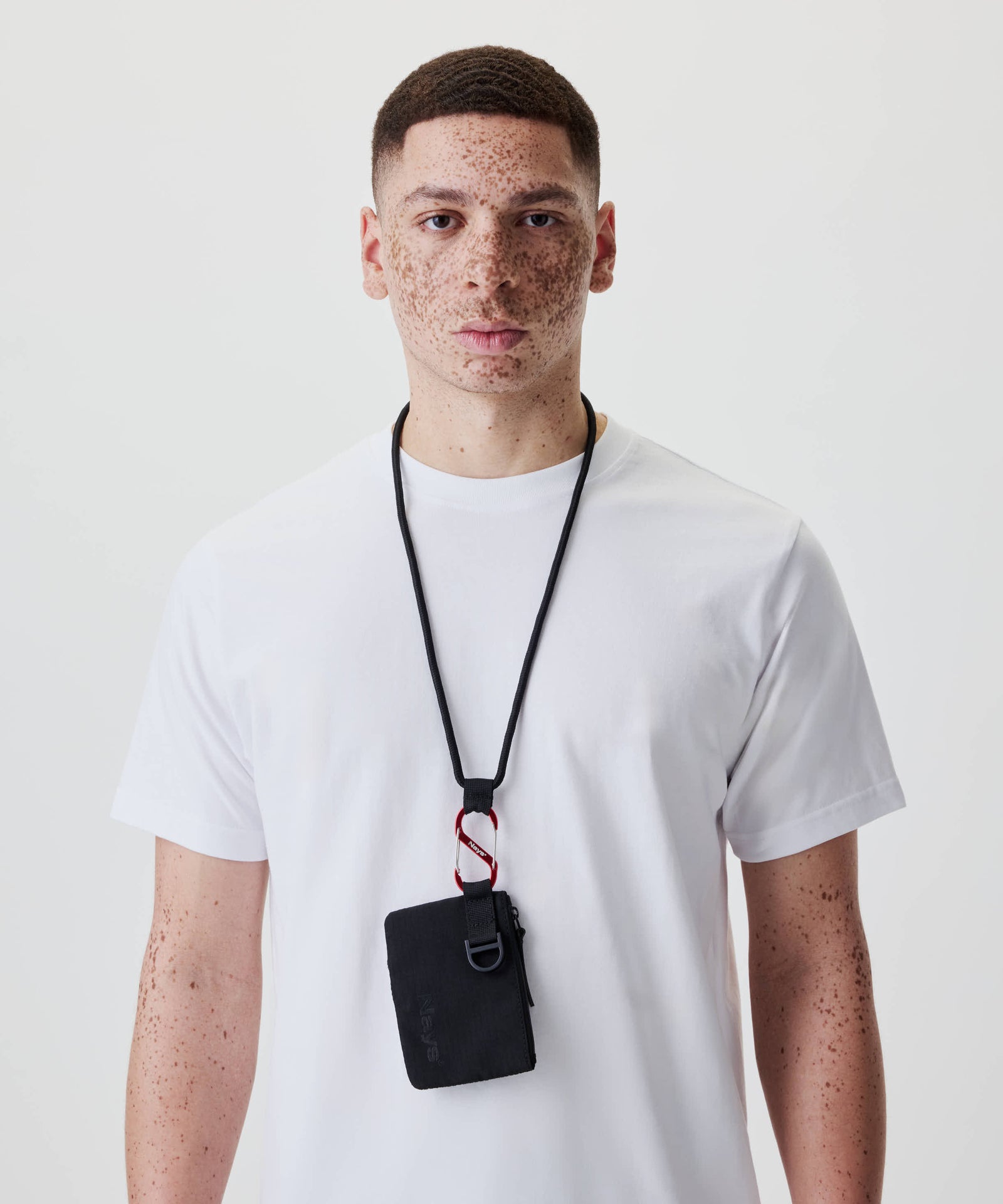 Ein junger Mann trägt das Nays Neck Pouch aus Ripstop, mit Reißverschlussfach und Mesh-Tasche, an einem schwarzen Band um den Hals.