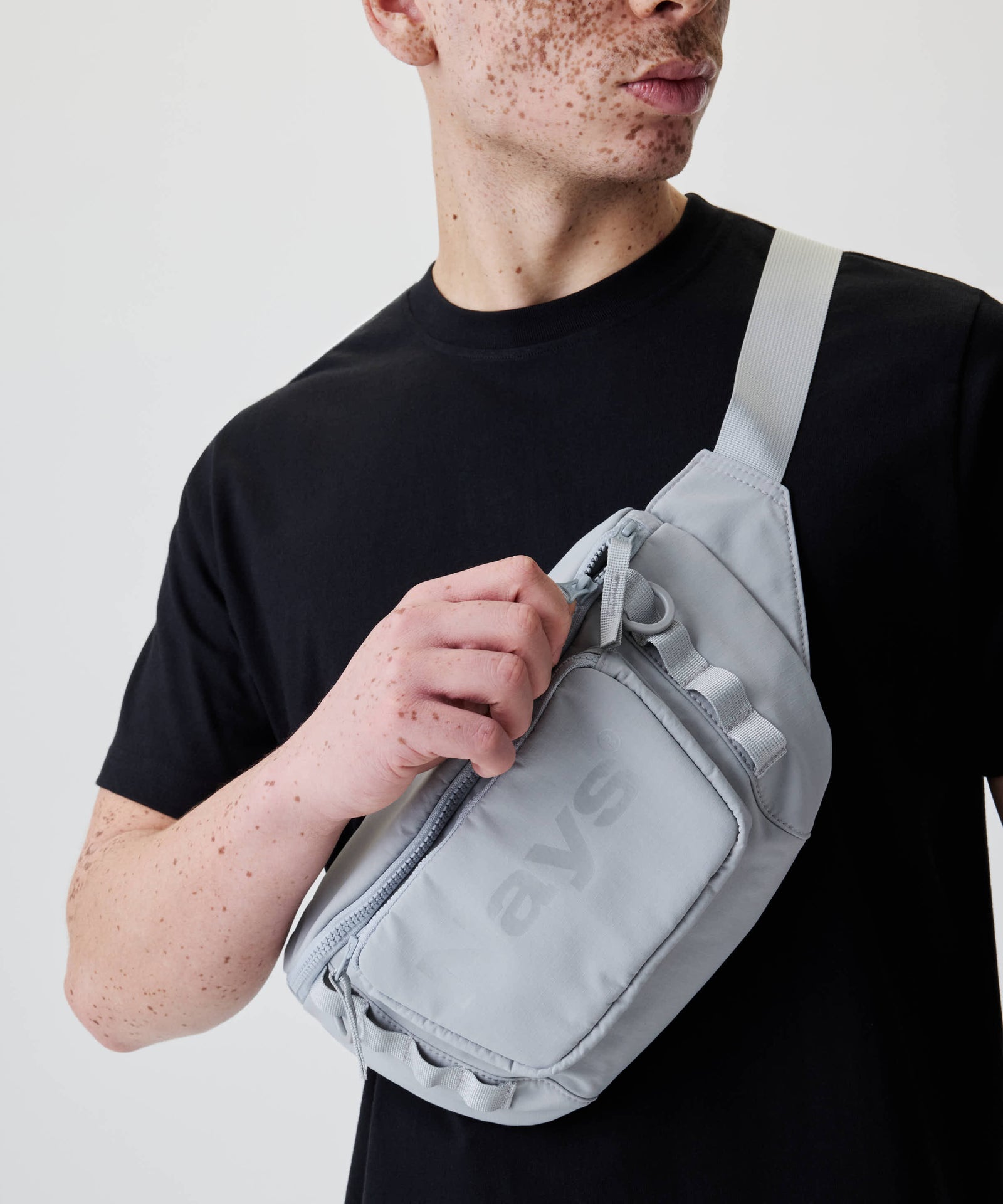 Person trägt die Nays Lightweight Cross Body Bag aus Nylon mit Hand am Frontfach-Reißverschluss, zeigt Schlaufen, D-Ringe, und verstellbaren Gurt.