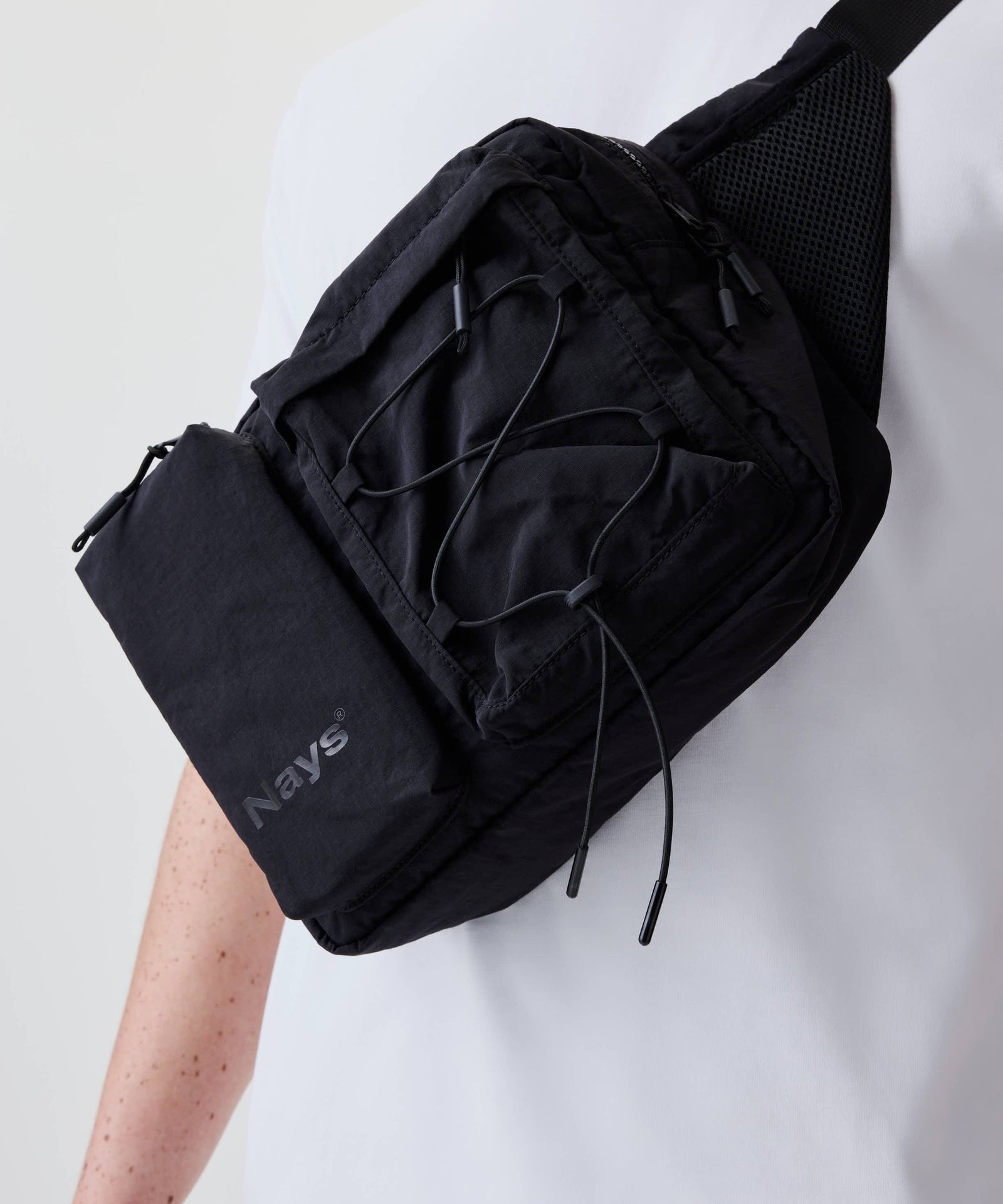 Person trägt die Nays Utility Cross Body Bag 2.0 mit mehreren Reißverschlussfächern und elastischem Kordeldetail, ideal für vielseitige Nutzung und sicheren Stauraum.