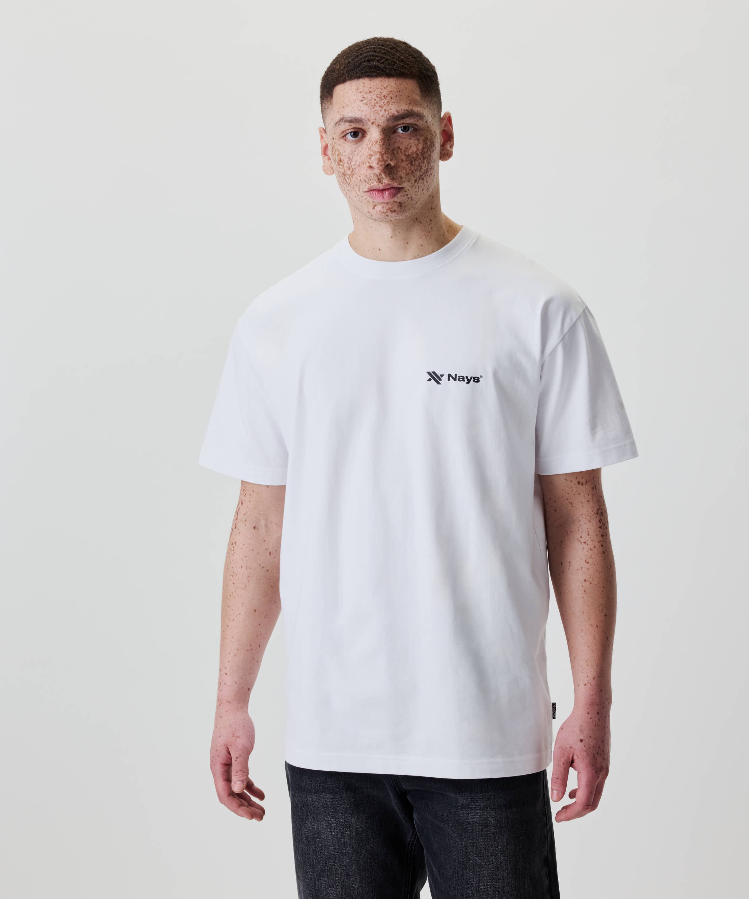 Ein junger Mann trägt das Nays Loose Fit Chest Print Tee, ein lässig geschnittenes, weißes T-Shirt mit kleinem Logo auf der Brust.