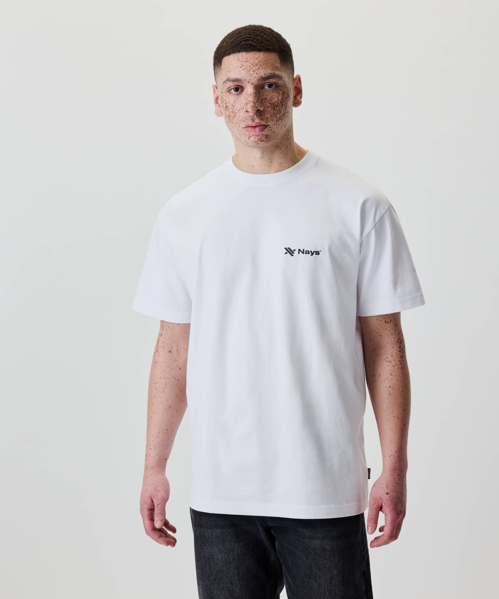 Ein junger Mann trägt das Nays Loose Fit Chest Print Tee, ein lässig geschnittenes, weißes T-Shirt mit kleinem Logo auf der Brust.