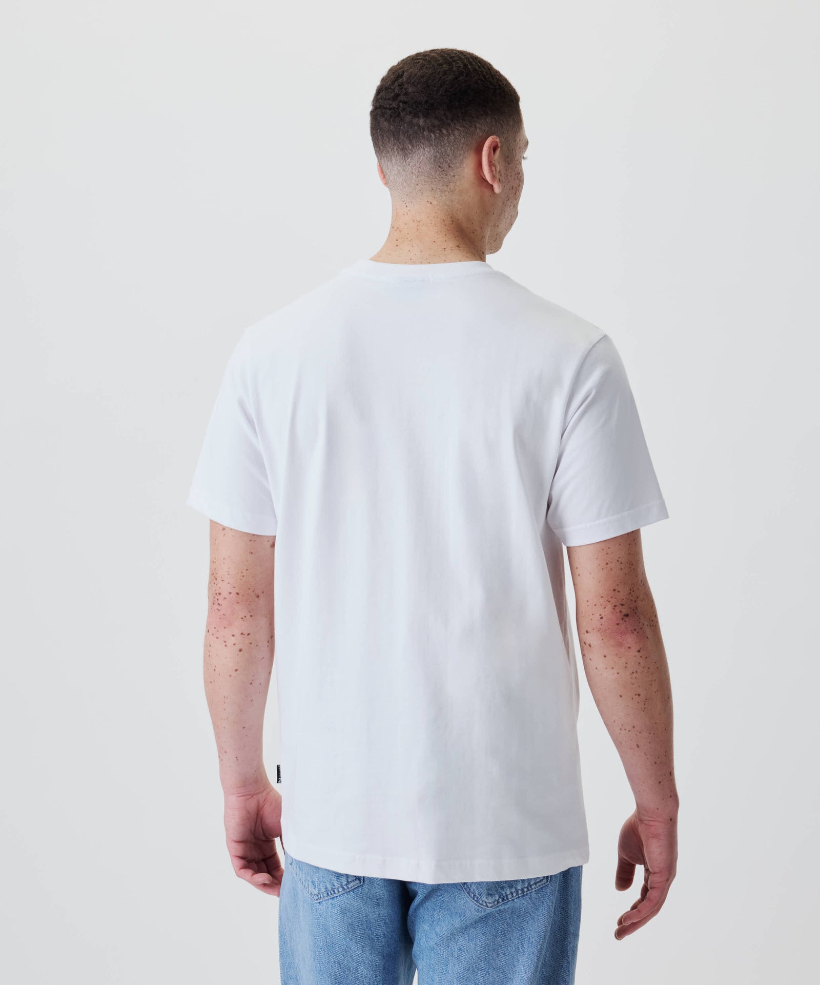 Person in Nays Classic Regular Flag Tee, weiß, mit kurzem Haar, von hinten. Das T-Shirt hat reguläre Passform, keine Logos, ideal für den Alltag.